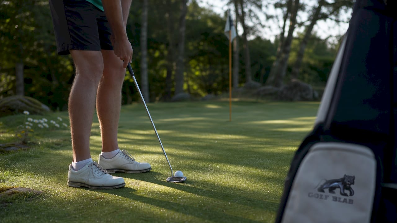 Golfer making putting stroke on green near hole