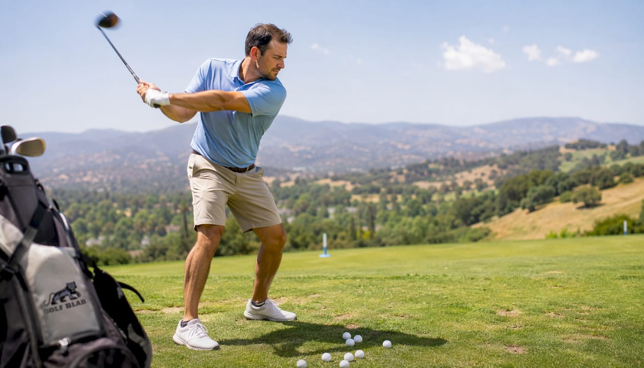 Golfer mid-swing on driving range at dawn