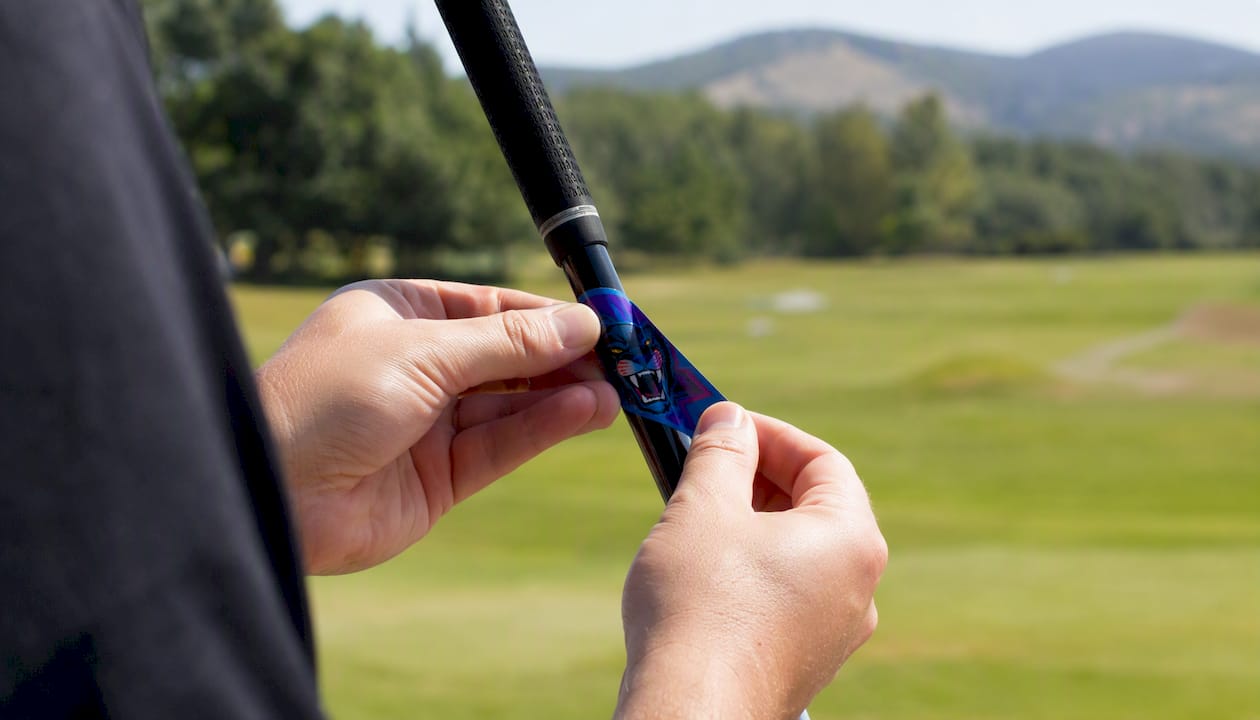Hands applying custom golf club label outdoors