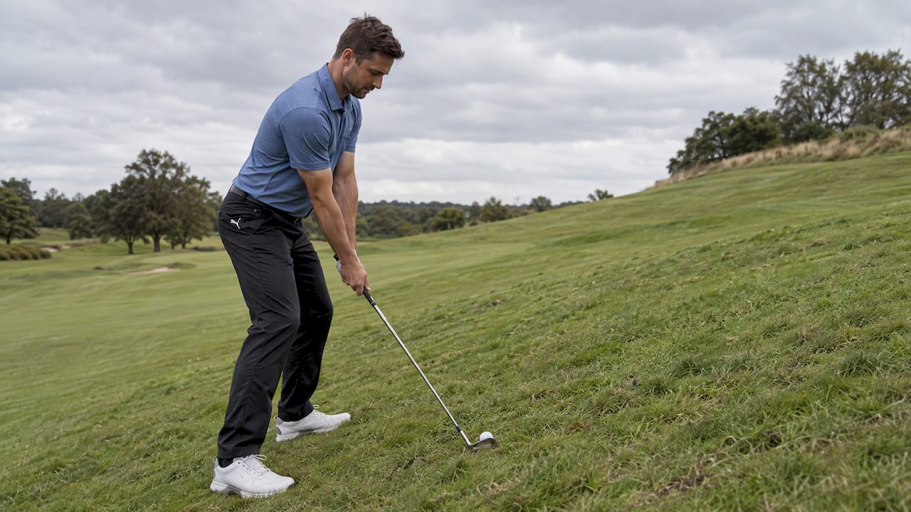 Golfer addressing ball on sloped fairway