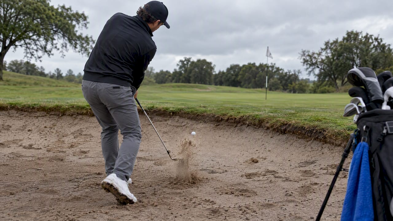 Golfer striking ball from wet bunker